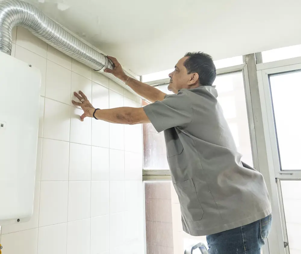 Técnico ajustando o duto de exaustão de um aquecedor a gás na parede de azulejos brancos
